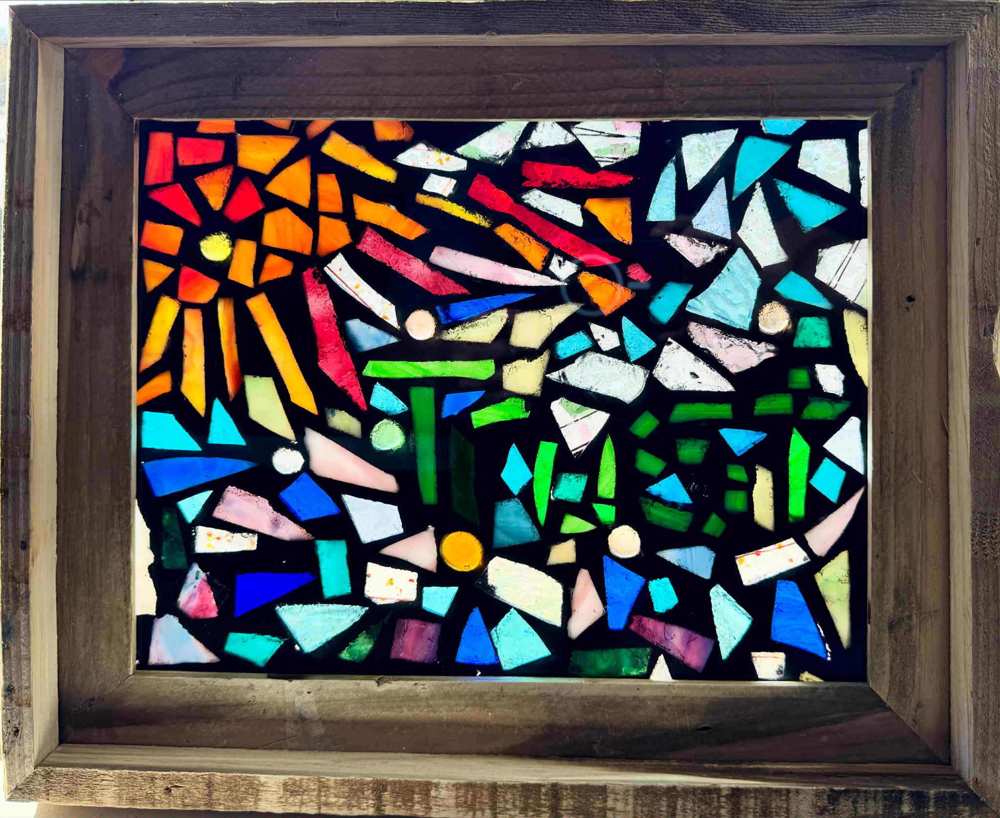 Colorful mosaic artwork framed in wood, featuring a radiant orange sun with rays, deep blue ocean waves, and vibrant green shapes representing growth and life—symbolizing trust, light from Jesus Christ, and the grandeur of God’s creation.
